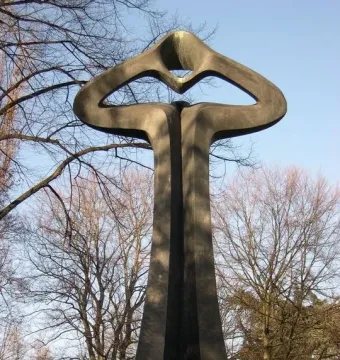 Der Mahner, a tall dark abstract sculpture with a tapering base and open upper form standing on grass.