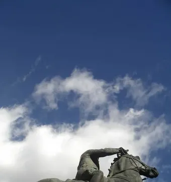 Dark bronze equestrian statue of Francisco Franco against a blue sky with scattered clouds.