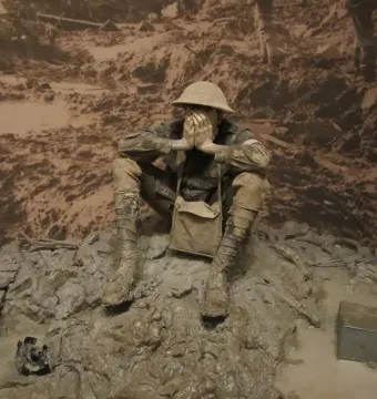 Man in the mud sculpture of a soldier sitting with hands covering his face in muddy terrain.
