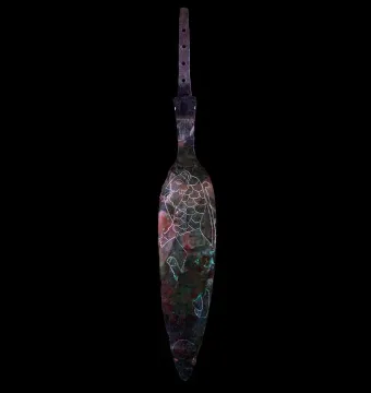 The Spear of Lugal, a weathered dark metal blade with a perforated tang and engraved animal figure against a black background.