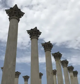 Weathered Capitol Columns stand in a row against a partly cloudy sky.