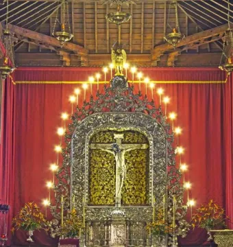 Cristo de La Laguna crucifix centered in an ornate gilded altar with lit candles and red curtains