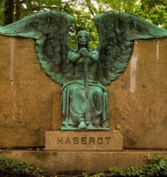 Weathered green Haserot Angel statue with large wings mounted on a granite monument.