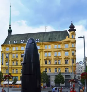 The Brno astronomical clock stands in a paved square with a yellow building and spire behind it.