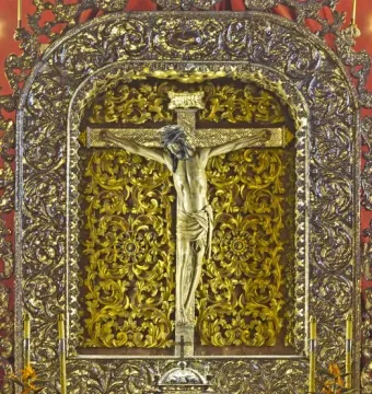 Cristo de La Laguna on the cross בתוך an ornate golden altar shrine with flowers below.