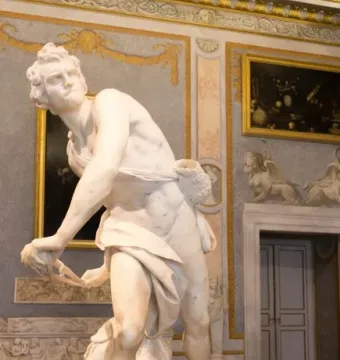 David marble statue in a gilded gallery, shown in a dynamic twisting pose with sling and draped cloth.