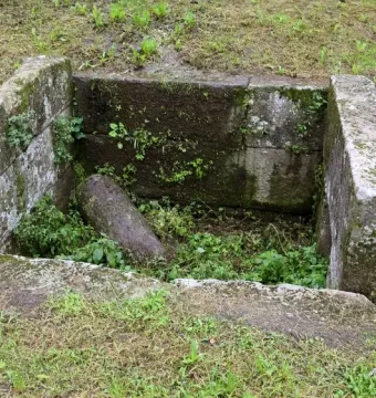 Sunken stone Etruscan tomb structure with moss and weeds growing over the weathered blocks.
