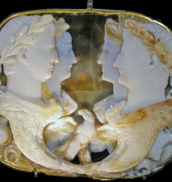 Gemma Claudia cameo with four profile portraits facing inward, gold border, and intertwined horn-shaped elements at the bottom.