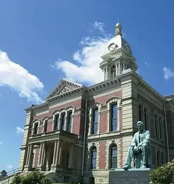 The Lincoln Monument stands in front of a large brick and stone courthouse with a clock tower.