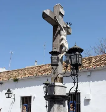 Christ of the Lanterns sculpture with a white crucified figure on a stone column, surrounded by black lanterns and iron fencing.