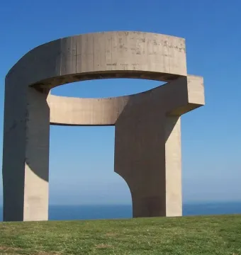 Elogio del Horizonte, a large concrete sculpture with a curved opening, standing on a grassy slope above the sea.