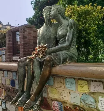 The Muretto of Alassio lovers statue, a bronze couple seated on a wall covered with colorful ceramic tiles and signatures.