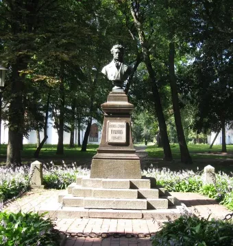 Bust of Pushkin on a tall pedestal in a green park with flowers and a brick path