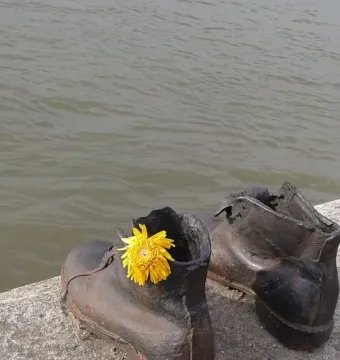 Shoes on the Danube Bank sculpture with two dark metal shoes on a concrete riverbank, one holding a yellow flower.