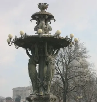 Bartholdi Fountain in a snowy park with a domed building visible through bare trees