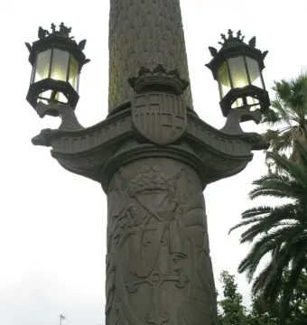 Galceran Marquet Monument detail showing a crowned coat of arms, heraldic reliefs, and two ornate lamps on ship-prow supports.