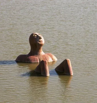 Hombre Río sculpture emerging from calm water with a peaceful face.