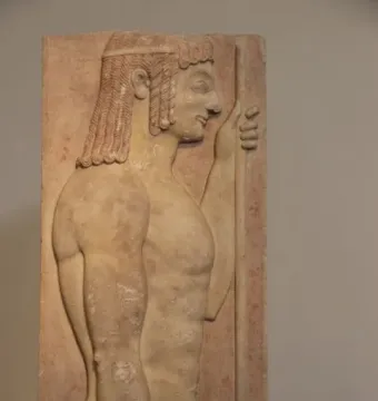 Parian Marble funerary stele of a young javelin-bearer carved in pale stone, shown in profile with curly hair and a staff.