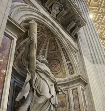 Saint Andrew stone sculpture in an ornate arched niche, holding a rough wooden post.