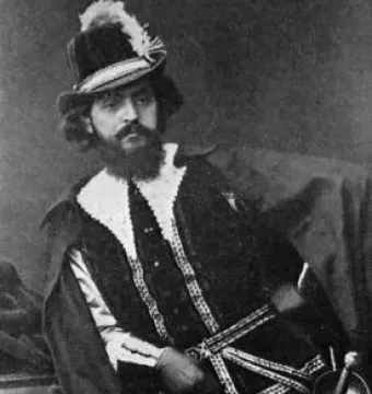 A black-and-white portrait of a man in elaborate theatrical costume with a feathered hat, ruffled collar, beard, and sword.