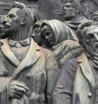 Weathered bronze relief on the Branting Monument showing a crowd of figures, including men with beards and a woman in a headscarf.