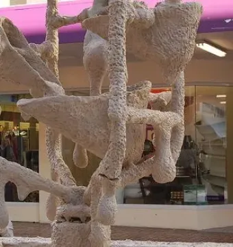 The Bucket Fountain sculpture with a rough off-white textured surface, bucket-like forms, and hanging drips, with part of a similarly covered car visible beside it.