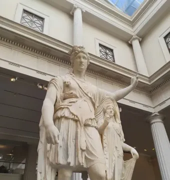 Hope Dionysus, a white marble statue of a standing classical figure with a raised left arm beside a smaller draped figure in a museum gallery.