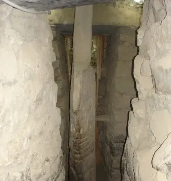 The Lanzón monolith standing in a narrow stone passage, with intricate carvings visible on its surface.