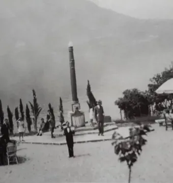 Lighthouse of Lierna standing by Lake Como with people gathered around it and mountains in the distance.