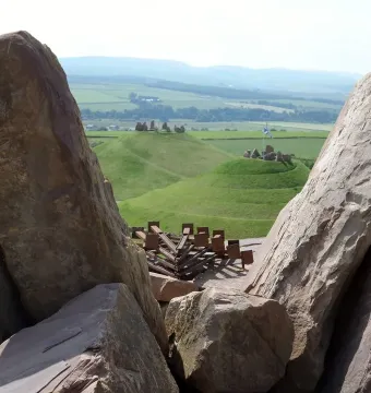 Rugged reddish-brown stones of the Omphalos frame rolling green hills and spiral terracing beyond.