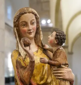 Painted wooden sculpture of the Virgin on a wide throne holding the child, with a fruit in her raised right hand.