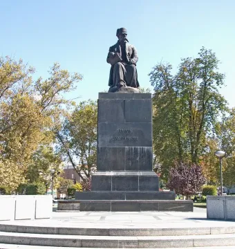 Vuk Karadžić Monument with a seated bronze figure holding a book on a tall stone pedestal surrounded by trees