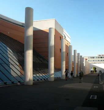 Tall pillars of the Way of Human Rights line a walkway beside modern buildings, with people walking through the installation.