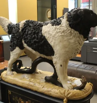 Bashaw, a sculpture of a black and white dog standing with its paws on a coiled snake in a museum display.