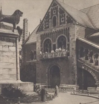 Brunswick Lion statue on a tall stone pedestal beside an ornate brick building.