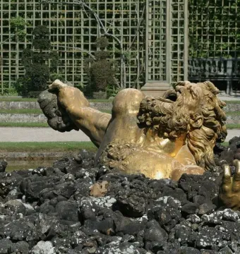 Enceladus Fountain sculpture of a golden bearded figure emerging from dark rocks in a garden setting.