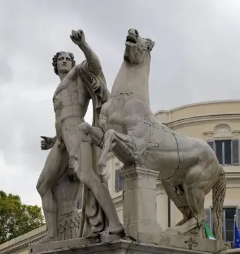 Marble horse tamer statue with a rearing horse on a stone pedestal against a cloudy sky.