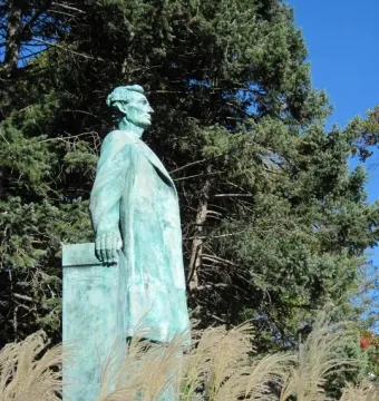 Lincoln the Lawyer bronze statue of Abraham Lincoln in a long coat, standing against a blue sky and evergreen trees.
