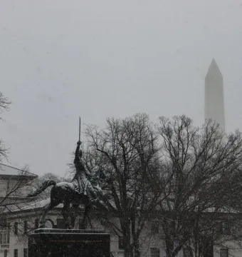 Simón Bolívar equestrian statue partly obscured by falling snow, with the Washington Monument in the background.