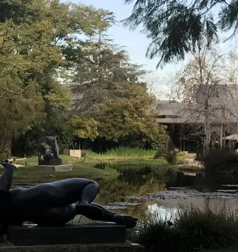 The River, a dark reclining female nude sculpture beside water with trees and other sculptures in the background.