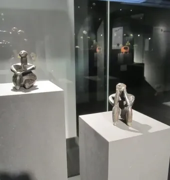 The Thinker of Cernavodă terracotta figurine displayed on a pedestal in a museum case, with a similar figure behind it.