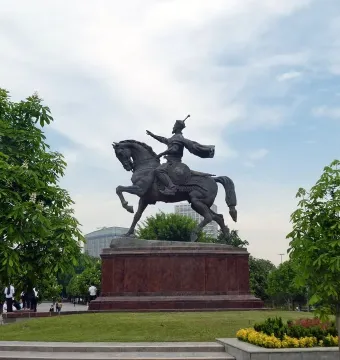 Timur Equestrian Statue on a reddish-brown pedestal in a green park with trees and flowering shrubs.