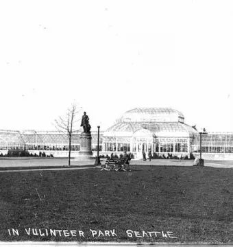 William Henry Seward statue on a pedestal in front of a glass conservatory in Volunteer Park.