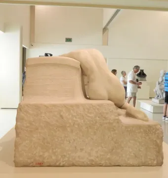 Desolation, a light stone sculpture of a reclining nude figure seen from the back on a rough rectangular base.