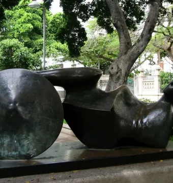 Goslar Warrior, a dark bronze reclining abstract sculpture with a circular disc on a rectangular base outdoors.