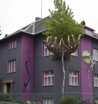 Kristek House with a dark gray facade, purple vertical stripes, golden hands, and surreal mural details.