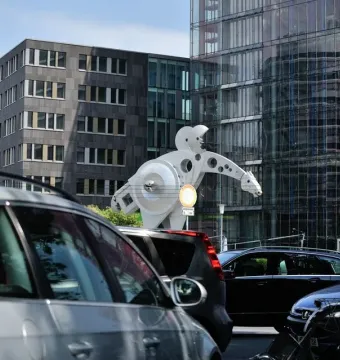 The S-Printing Horse sculpture stands beside modern buildings, partly hidden by parked cars.