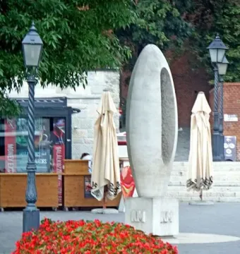 Zero Kilometre Stone sculpture beside a bed of red flowers with buildings and streetlights in the background.