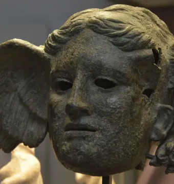Bronze head of Hypnos with a wing on the side, showing a tranquil face with wavy hair and a weathered surface.
