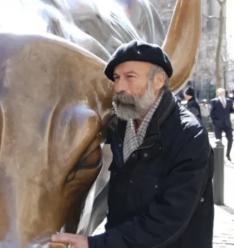 Arturo Di Modica stands beside the Charging Bull sculpture, touching its snout.